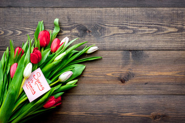 First spring flowers. Bouquet of colorful tulips near Spring is coming note on dark wooden background top view copy space