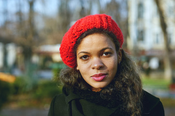 a young colored woman in the city .A woman in a red knitted beret on the street