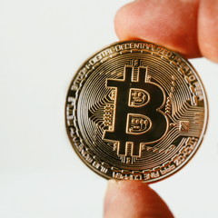 A golden bitcoin on a sheet of white paper is holding a finger. Bitcoin is a crypto currency. Bitocoin isolated on white background