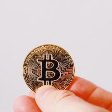 A golden bitcoin on a sheet of white paper is holding a finger. Bitcoin is a crypto currency. Bitocoin isolated on white background