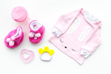 Cute pink baby clothes for girl. Shirt, booties, toy, bottle on white background top view copy space