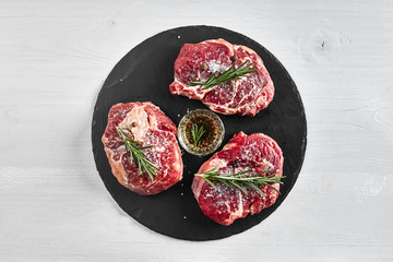 Fresh raw beef steaks with herbs, garlic, olive oil, pepper, salt and rosemary on black board: Tenderloin, Striploin, Rib Eye