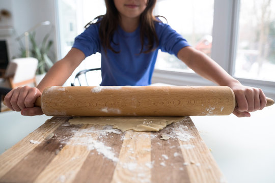 Young girl rolling out pastry with rolling pin.