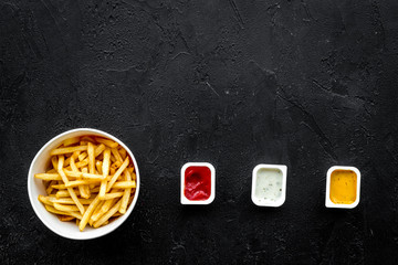French fries with sauces on black background top view copy space