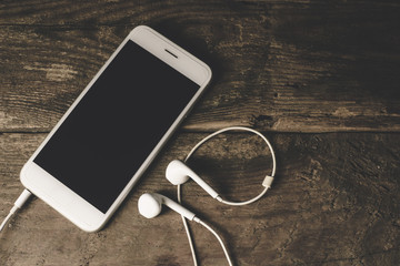 Close-up of smart phone with headphones on a Wood background. Listen to music. vintage Tone