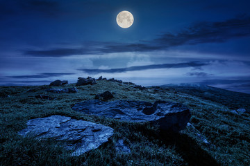 rocky formation on grassy hillside. beautiful scenery of Runa mountain in summertime at night in full moon light. location Carpathian mountains, Ukraine
