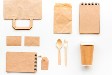 Disposable tableware. Paper cup, spoon, fork near brown paper bag, label and notebook top view mock up pattern white background