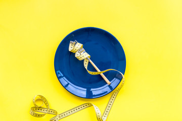 Medical starvation for lose weight. Empty plate, apple and measuring tape on bright yellow background top view