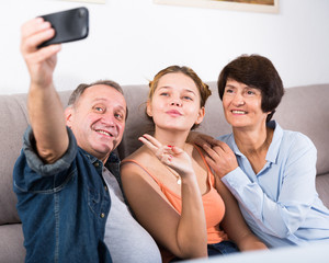 Marrieds with their adult daughter are takinf selfie together on sofa