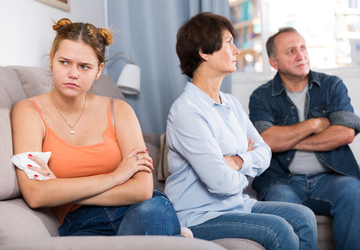 Adult couple is carefully talking with a sad daughter on sofa