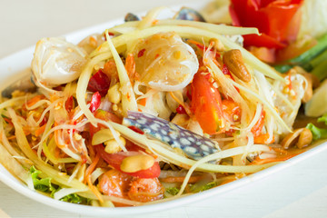 Thai papaya salad with field crab in white dish on the stone table.