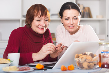 Mature woman and daughter at table using laptop