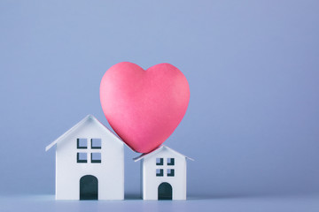 Two white origami houses with big pink heart on the roof on the blue background. Family story in...