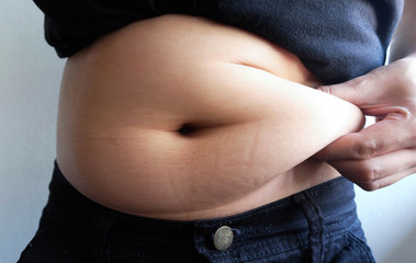 woman hand catching fat body belly paunch , diabetic risk factor 