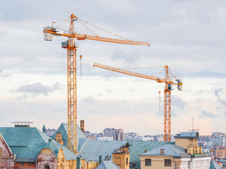 Pair of construction cranes upon roofs of building on historical center of Moscow. Industrial machinery on sunset cloudy sky background. Russia.