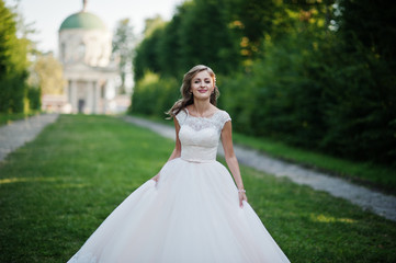 Lonely attractive bride walking on the green alley which leads to a church.