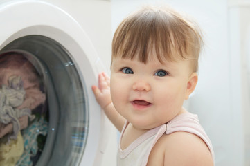 Baby portrait near washing machine looking at camera,  having fun and playing with washer