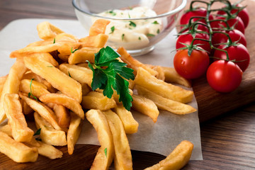 French fries, cherry tomatoes, garlic sauce on a wooden brown background, close-up. Fast food.
