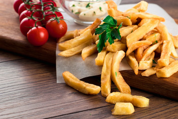French fries, cherry tomatoes, garlic sauce on a wooden brown background, close-up. Fast food.