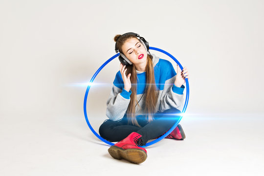 Cool young woman listening to music on headphones, with blue hula hoop and red shoes and lipstick