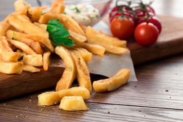French fries, cherry tomatoes, garlic sauce on a wooden brown background, close-up. Fast food.