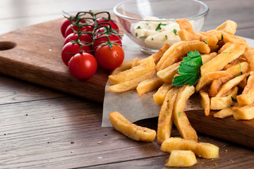 French fries, cherry tomatoes, garlic sauce on a wooden brown background, close-up. Fast food.