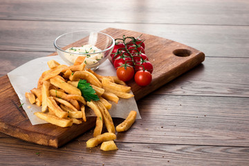 French fries, cherry tomatoes, garlic sauce on a wooden brown background, close-up. Fast food.