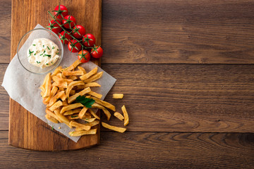 French fries, cherry tomatoes, garlic sauce on a wooden brown background, top view. Fast food.