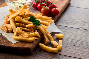 French fries, cherry tomatoes, garlic sauce on a wooden brown background, close-up. Fast food.
