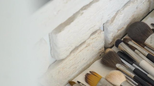 On table is a set of brushes for make-up from different wool. Near brick wall an even number of tools for applying cosmetic powder and foundation.