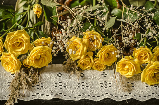 Black plywood with a white embroidered border lie yellow roses with dry twigs of white gypsophila and reeds
