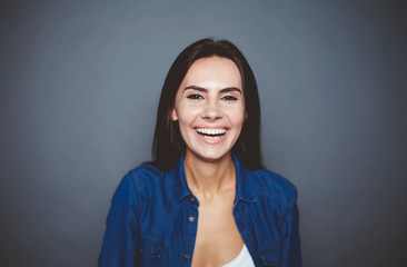 Fototapeta premium Portrait of a beautiful smiling modern girl in a denim shirt which poses in front of the camera on a gray background isolated.