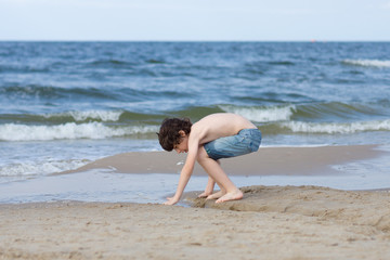 Fototapeta na wymiar A guy in denim shorts is happy on the sandy beach of the sea.