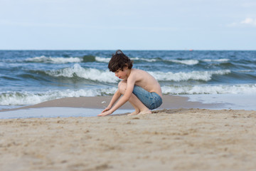 Fototapeta na wymiar A guy in denim shorts is happy on the sandy beach of the sea.