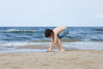 A guy in denim shorts is happy on the sandy beach of the sea.