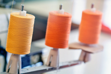 Closeup of three thread coils for industrial sewing machine of bright orange color.
