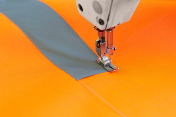 Closeup of sewing machine head and orange fabric for special protective clothing bright orange.