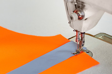 Closeup of sewing machine head and orange fabric for special protective clothing bright orange.