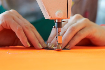 Closeup of a tailor's business - female hands behind her sewing on a sewing machine in the workshop.