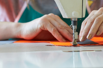 Closeup of a tailor's business - female hands behind her sewing on a sewing machine in the workshop.