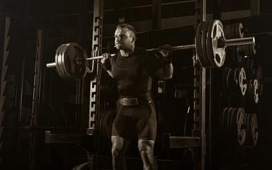 The weightlifter stands with a very heavy barbell on his shoulders.