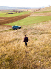 A girl going towards a car in a field . drone portait shot of a girl in a field