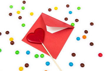Gift for Valentines day. Red lollipop in the shape of a heart on the white background with colorful button-shaped chocolates and red envelope.