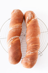 Rustic artisan French baguette home made from whole wheat and regular bread bread flour, water, yeast and sourdough fresh from the oven on cooling rack on white wooden kitchen table