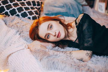 молодая красивая девушка с татуировками на руках лежит на кровати young beautiful girl with tattoos on the hands lying on the bed - obrazy, fototapety, plakaty