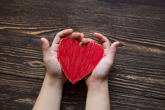 Children's hands giving red heart on a wooden background.