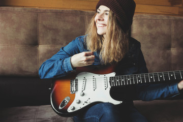 Young woman playing guitar and smiling. Music concept. Home atmosphere on background.