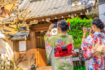 Fototapeta na wymiar Japanese women in kimono take picture of Yasaka Shrine also known as Gion Shrine, one of the most famous shrines in Kyoto, Japan, between Gion District and Higashiyama District. Springtime.