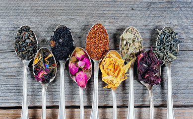 Various kinds of tea in spoons on wooden background. Dry Tea assortment.