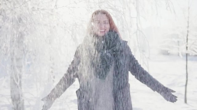 Young woman throw up a handful of snow and laughs, sunny winter day